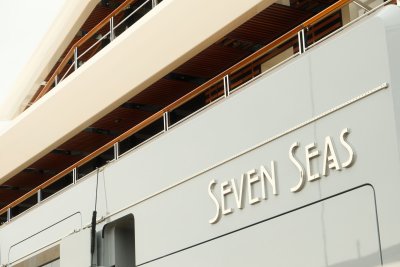 A large modern superyacht with white hull and multiple decks, moored at a marina with other boats visible