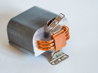 Close-up of a small semiconductor module sandwiched between a metallic heat sink and a flat heating surface, with wires attached