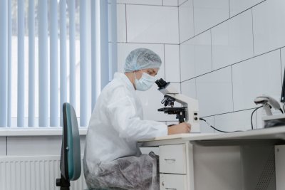 A scientist in a lab coat and safety glasses examining samples under a microscope in a modern research laboratory setting